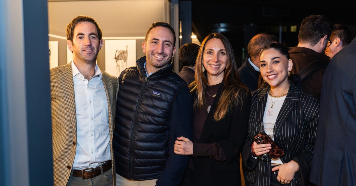 Four adults posing together at a social event, smiling at the camera in smart casual attire.